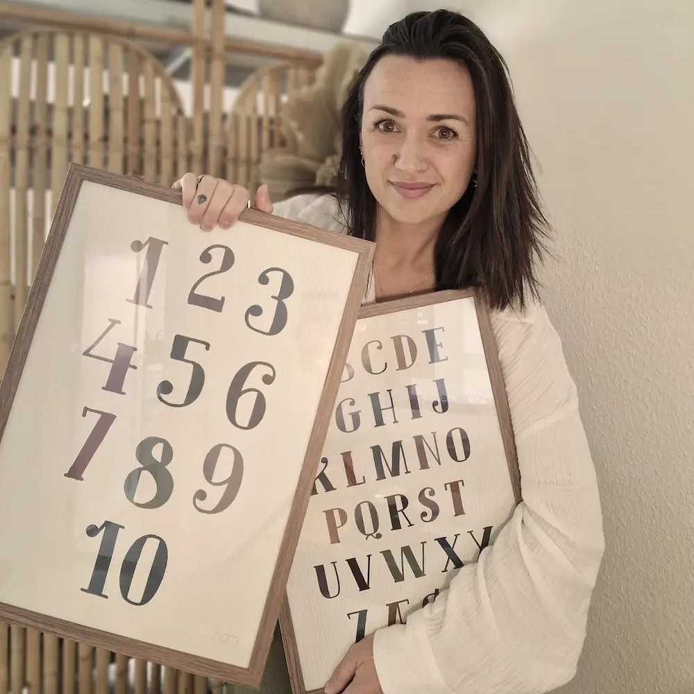 Denise, ejer af Nomi Creations. Står med læringsplakater til børneværelset